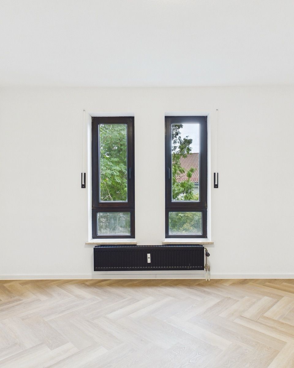 Leeres, frisch saniertes Zimmer mit Fischgrätparkett und zwei Fenstern